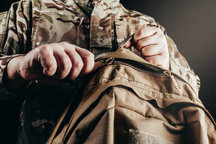 soldier in camouflaged uniform holding and unzipping backpack