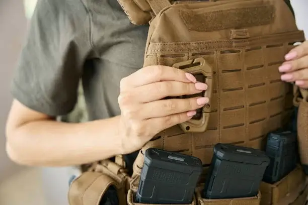 A person adjusts a tan plate carrier with MOLLE webbing, holding magazine pouches, on their back.