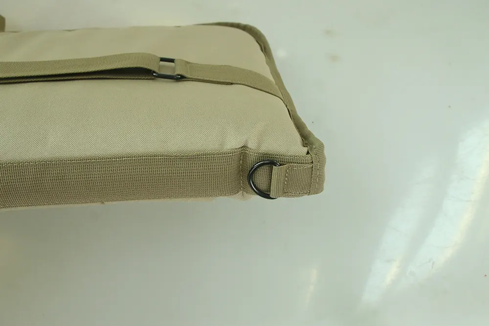 Close-up of a tactical gear strap with a black metal buckle and D-ring, sewn onto a beige fabric surface with reinforced stitching.