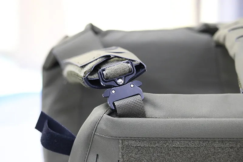 Close-up of a green tactical vest strap with a black quick-release buckle.