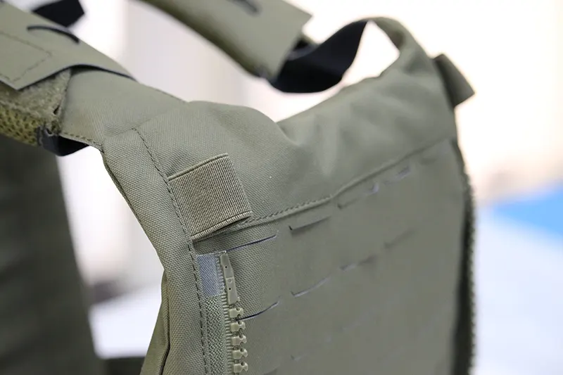 Close-up of a green tactical vest with MOLLE webbing and a side zipper.