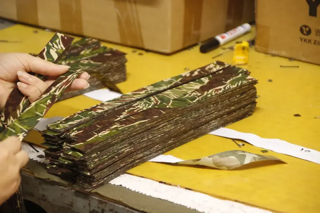 Skilled worker handling cut camouflage fabric strips on a worktable.